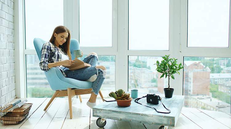 一位女士坐在窗前的椅子上看书，因为买了一套公寓而显得很开心.